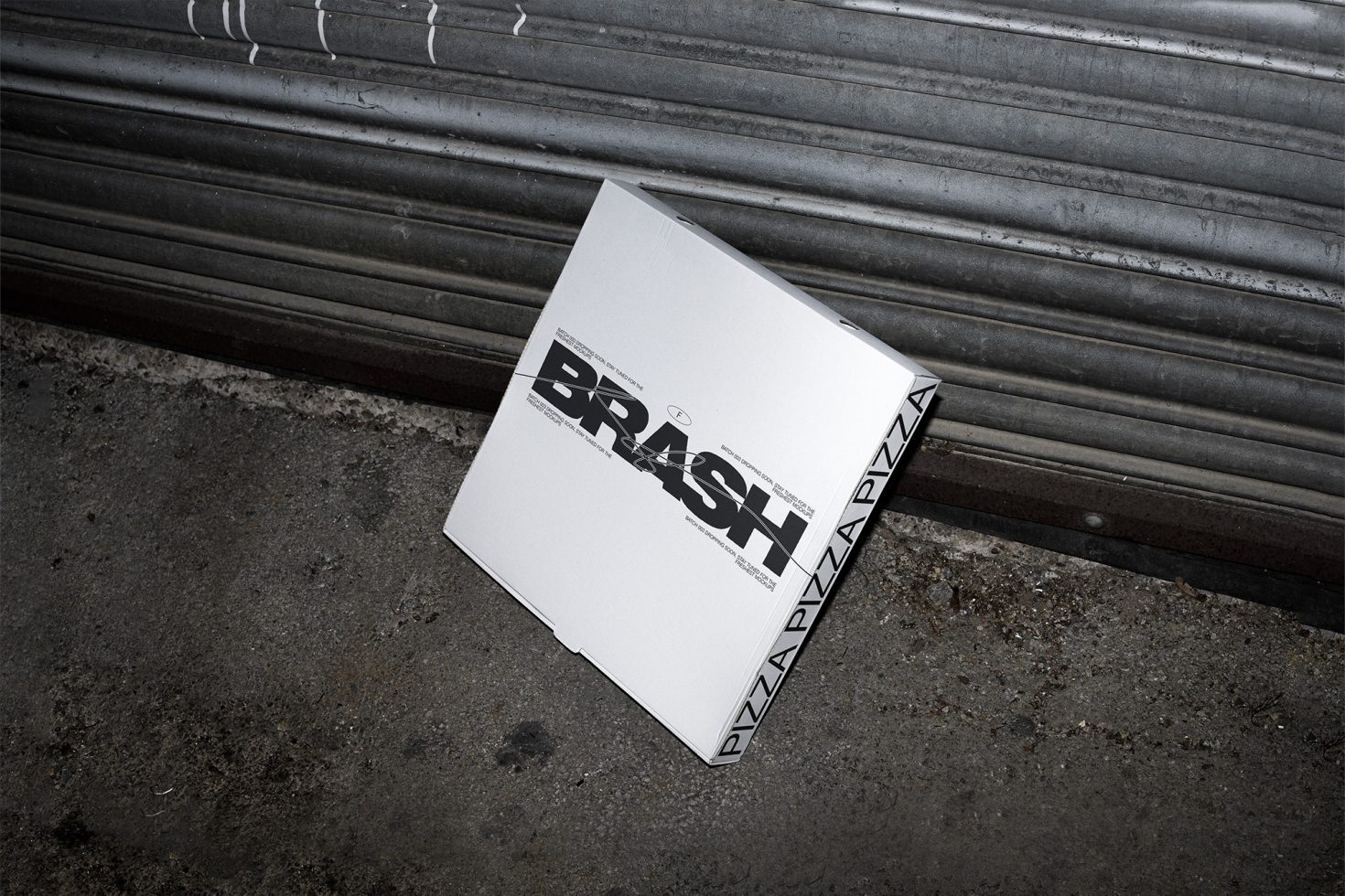 Urban style pizza box packaging mockup on concrete floor with metal shutter background, showcasing bold typography design.